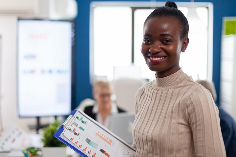 African woman manager looking at camera smiling, holding clipboard